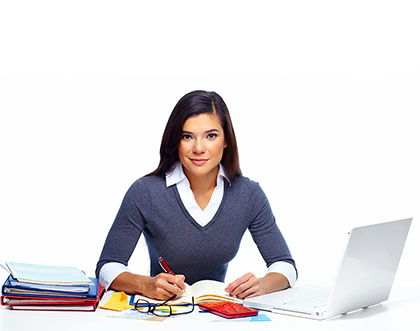 woman sitting in front of a desk with some binders, eye glasses, and laptop computer